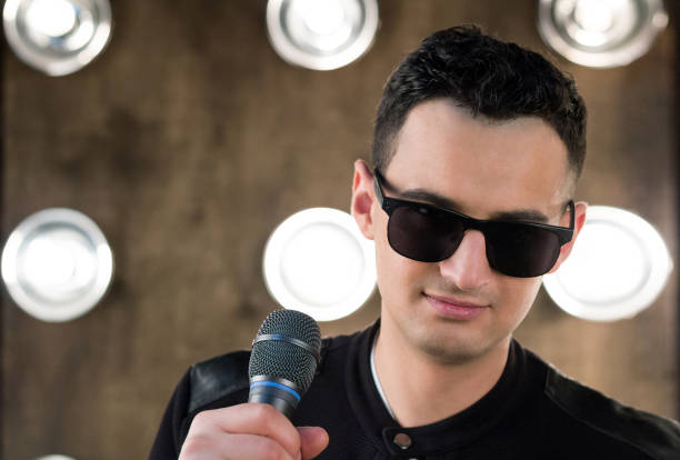 istock Male singer in sunglasses with microphone performing in projectors lights 641581660