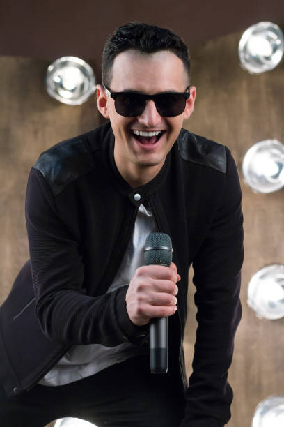 istock Male singer in sunglasses with microphone sings in projectors lights 641581938