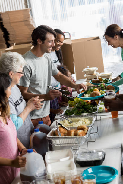 Friendly volunteers serve people in soup kitchen Diverse male and female volunteers serve healthy meals in homeless shelter or soup kitchen. Trays of food are on the table. serving size photos stock pictures, royalty-free photos & images