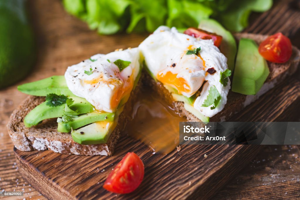 Tasty sandwich with poached egg and avocado Poached egg, avocado snack toast sandwich on wooden cutting board. Close up view, selective focus Egg - Food Stock Photo