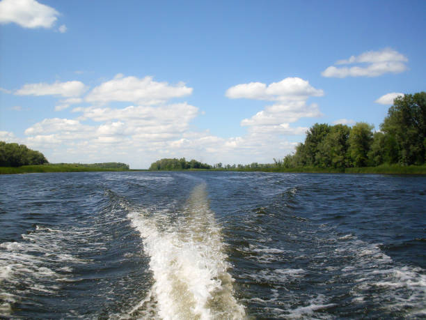 A Wake on the water from boats. The Volga River, Russia. Summer Sunny day, river landscape, blue sky, clouds, Islands