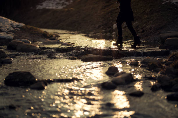 Young woman from behind at a stream in late Winter. Sunset in the background
