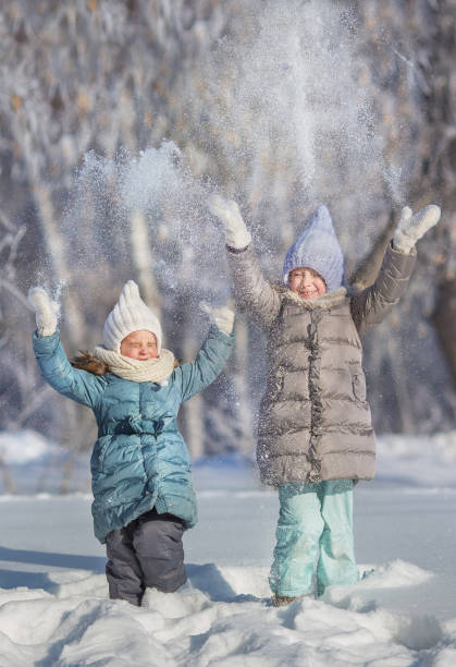 istock Two little sisters play and throw up a snow in winter 641639422