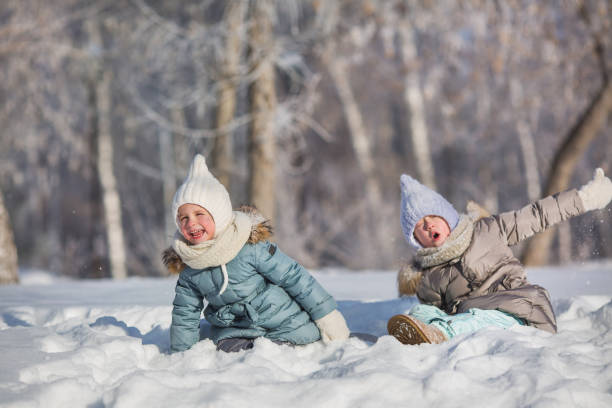 istock Two little girls sit in snowdrift and make faces in winter 641639636