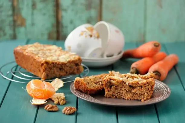 Homemade carrot cake with fresh carrots and clementines on turquoise background