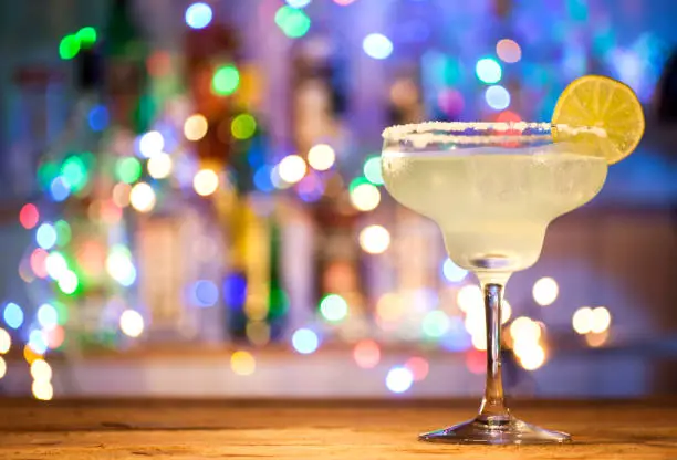Glass of margarita cocktail on bar lights background.
