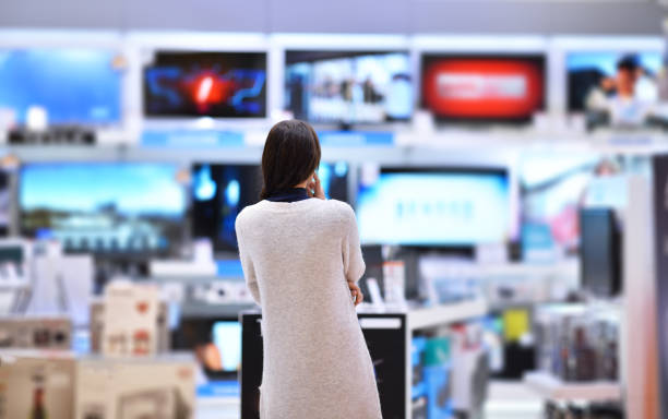Woman buys the TV A woman looking at a wall of televisions electronics store stock pictures, royalty-free photos & images
