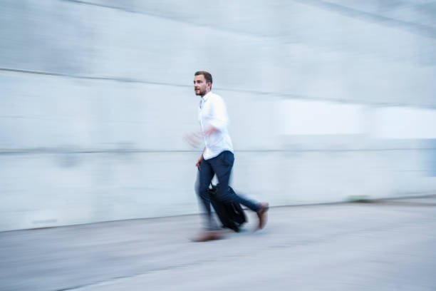 Businessman running with his suitcase in front of office building. Motion blur because of the motion of the camera and person movement.
