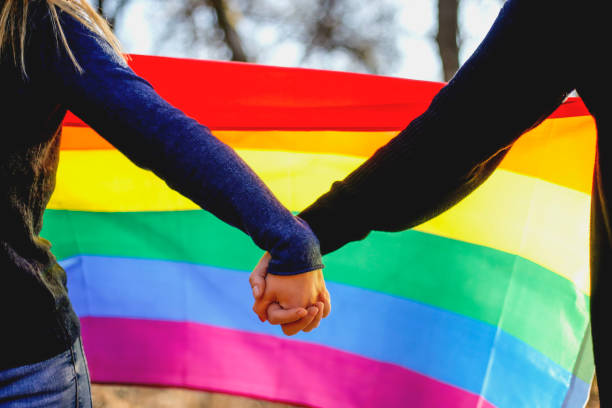 due ragazze lesbiche che si tengono per mano e bandiera arcobaleno - homosexual beautiful sensuality love foto e immagini stock