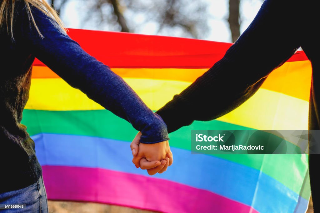 Two lesbian girls holding hands and rainbow flag LGBTQIA Culture Stock Photo