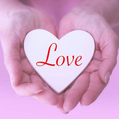 closeup of womans hands with white heart and the word Love