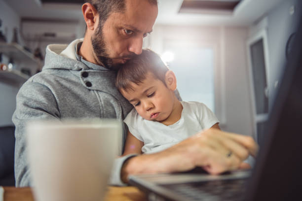 Father working on laptop and holding son on his lap Father working on laptop at home office and holding son on his lap single father stock pictures, royalty-free photos & images