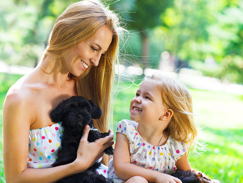 Cute little girl and her mother hugging dog puppies. Friendship and care concept