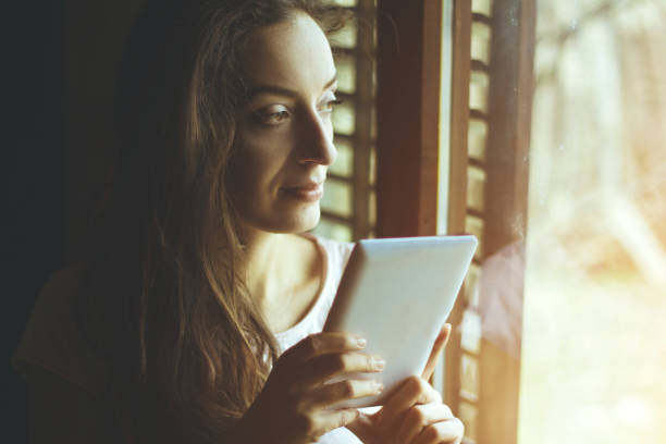 istock young woman using a tablet in the front of the window 641688056