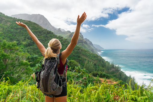 A young women hiker with arms raised looking upon the gorgeous view.