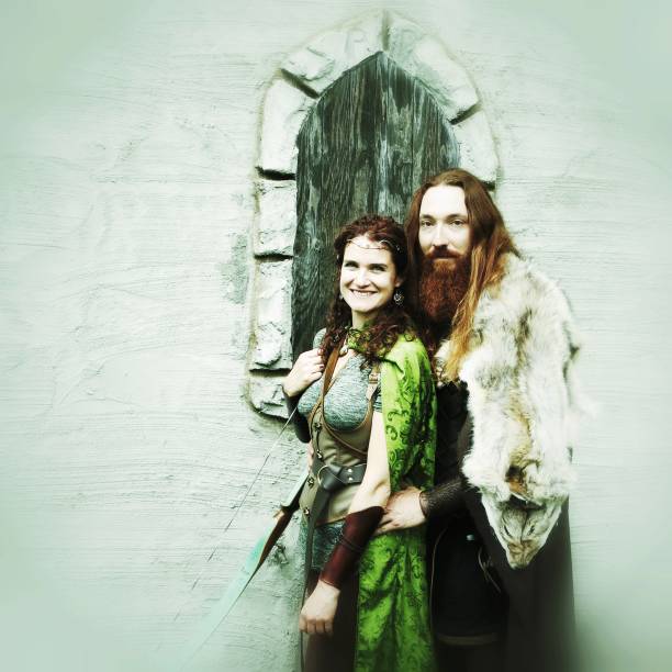 Two male Viking warrior men in authentic garb and armour travel in the forest with a female wood elf fairy fantasy character.Viking Norse Medieval Mythology, Warrior, Female Elf Relationship. Viking warrior and elf couple standing in front of castle facade.