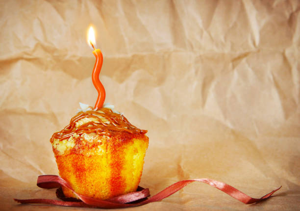 Birthday cake with one burning candle on brown paper background