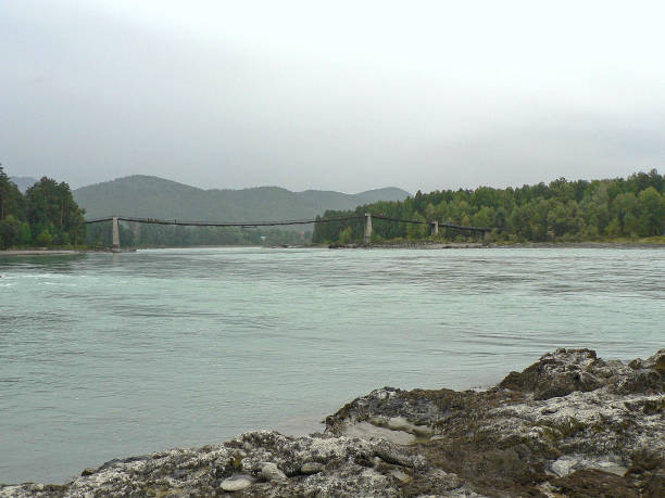 istock Mountain river. Rocks at front, suspension bridge at horizon. 641710018
