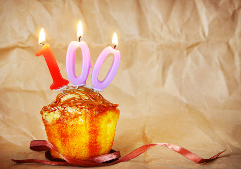 Birthday cake with burning candles as number one hundred on brown paper background
