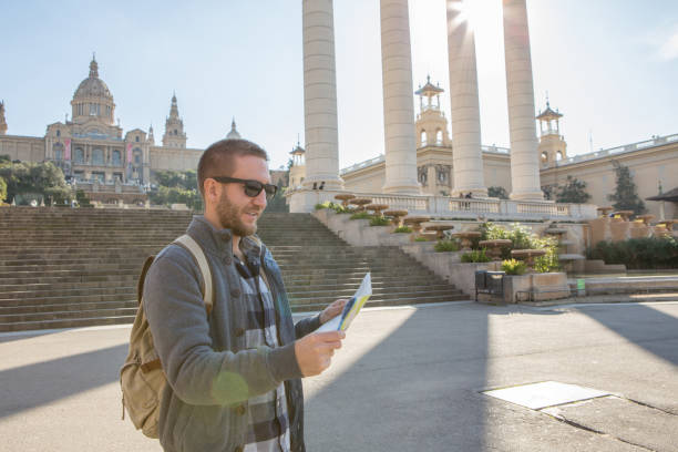 man with a map. Front view. The tourist in the denim jacket is angry or surprised. Isolated on white background. Young guy in tattoos with a map and binoculars looks indignantly