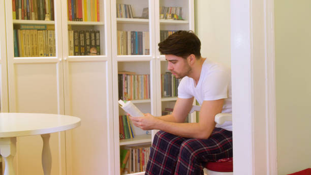 istock Young man reading a book in the home library 641728978
