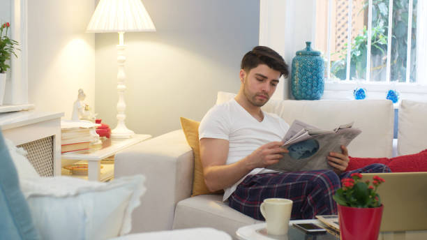 居間で新聞を読んでいる若い男の人 - young adult reading newspaper the media ストックフォトと画像