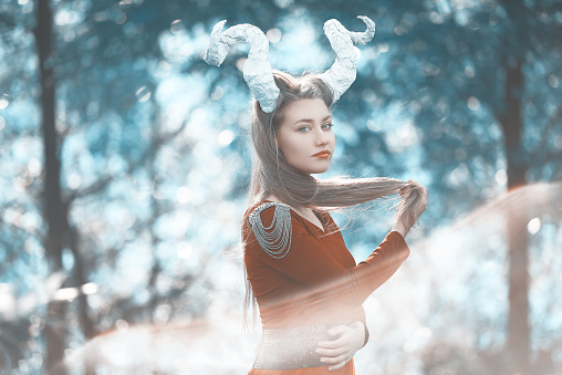 surreal woman in the forest wearing horns, posing in the sunset lights.
