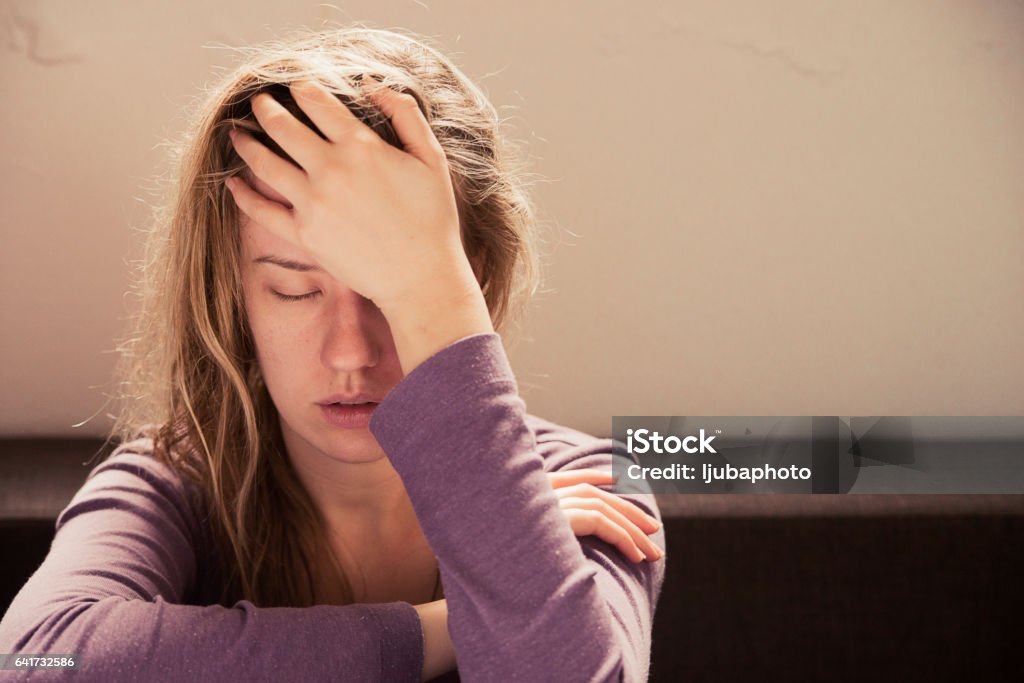 Woman suffering from stress or a headache grimacing in pain Lonely sad woman deep in thoughts sitting daydreaming or waiting for someone  in the living room with a serious expression,  she is pensive and suffering from insomnia sitting on couch Women Stock Photo