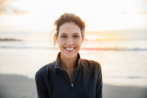 Portrait of happy female athlete at beach during sunset. Confident young woman is against sky on shore. She is sportswear.
