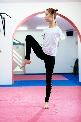 Portrait of determined young woman born with no upper limbs exercising taekwondo, stretching and kicking, expressing mental and physical strength