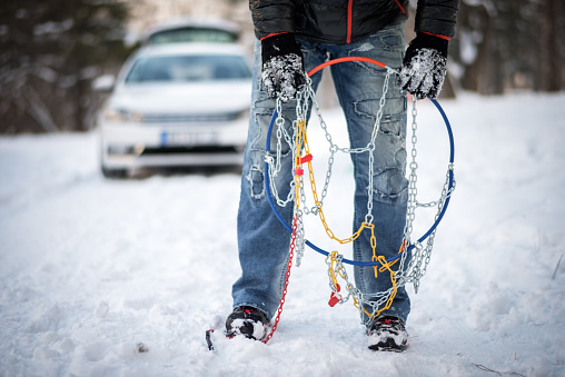 Uknown person is holding snow chains. White car is in the background.