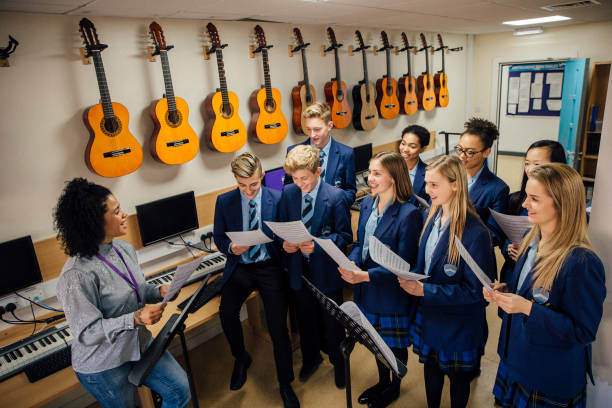 Singing In Music Lesson Class of teens are in their music lesson at school. There is a female teacher and the class are practicing choir with her. school choir stock pictures, royalty-free photos & images