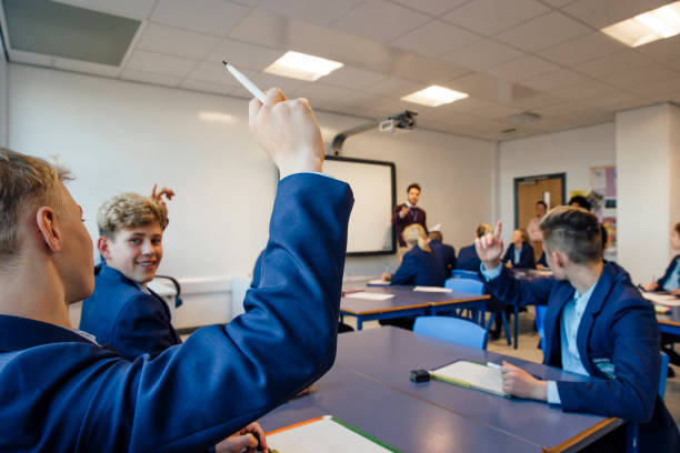I Know The Answer! Point of view shot of a high school lesson where the teacher has asked a question and some students have their hands up to answer. hand raised classroom student high school student stock pictures, royalty-free photos & images