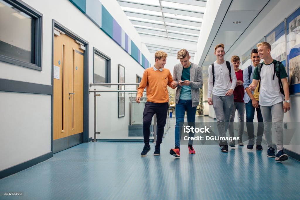 It's Break Time Group of teenage boys are walking down the school hall together to go for their lunch break. They are talking and laughing and some of the boys are using smart phones. School Building Stock Photo