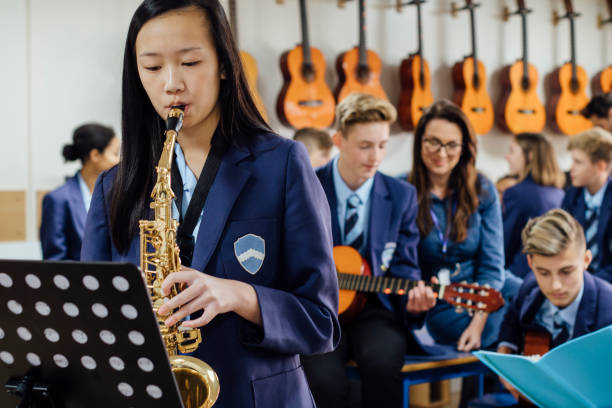 Playing The Saxaphone Teen student is playing the saxophone in her school music lesson. The rest of the class are in the background, out of focus. school uniform music lesson stock pictures, royalty-free photos & images