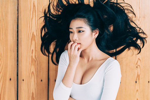 Portrait of young beautiful asian woman, lying on wooden floor contemplating.