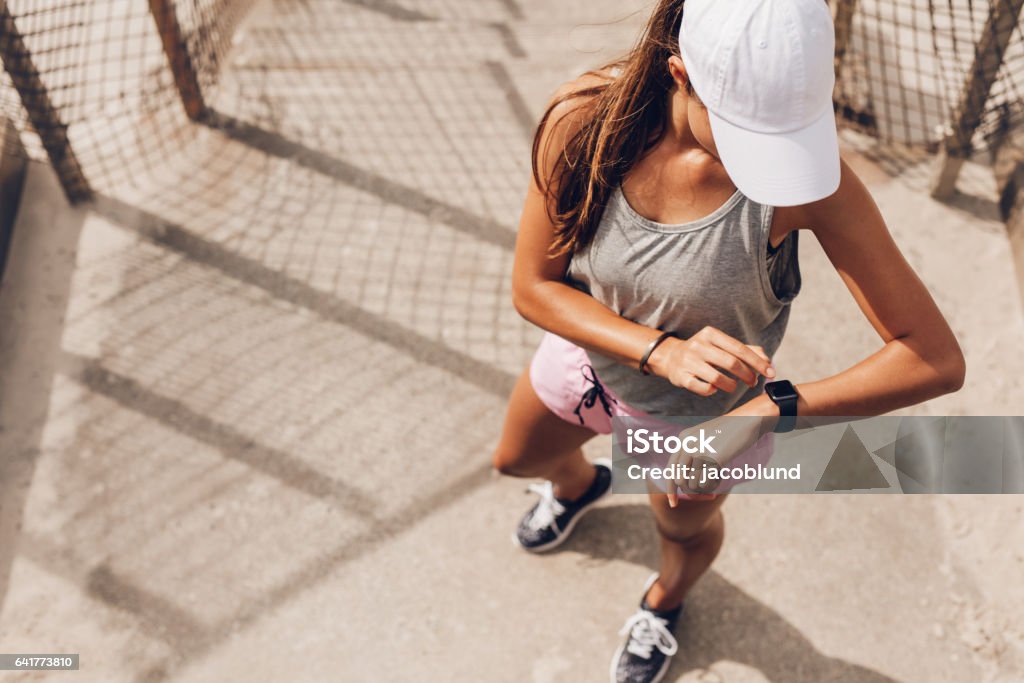 Female runner looking at smart watch heart rate monitor Young woman checking progress on smart watch. Female runner looking at smart watch heart rate monitor. Running Stock Photo