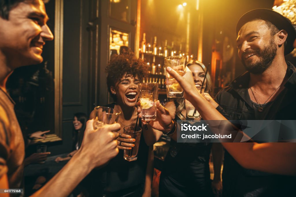 Young men and women enjoying a party Shot of young men and women enjoying a party. Group of friends having drinks at nightclub. Bar - Drink Establishment Stock Photo