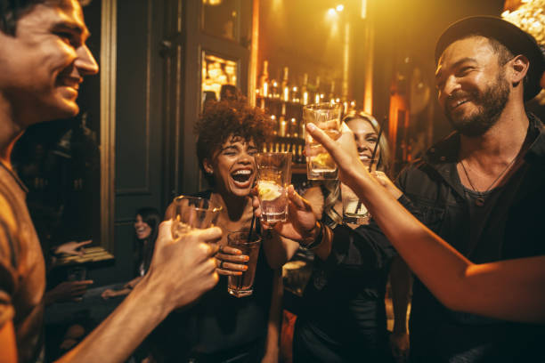 Young men and women enjoying a party Shot of young men and women enjoying a party. Group of friends having drinks at nightclub. cheers stock pictures, royalty-free photos & images