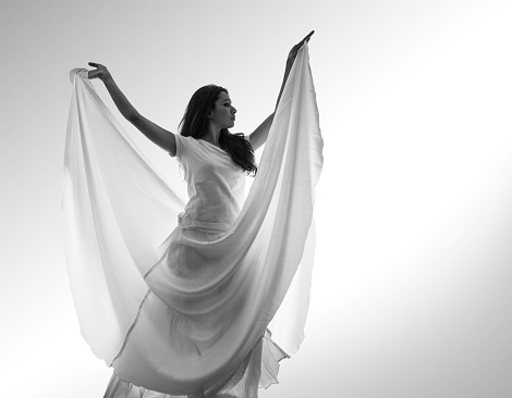 Young woman in white dress in Sufi dance pose against white background. grainy B&W image processing for mystical look.