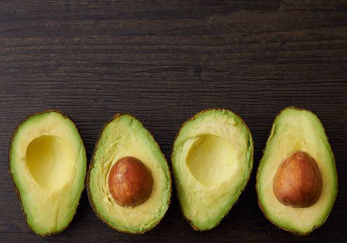 Avocado halves placed in a row on a wood surface