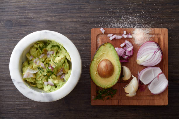 Authentic guacamole being made Chunky Guacamole in a marble bowl with avocado, garlic, cilantro, onion and salt on a wooden cutting board beside it. kosher starter recipes stock pictures, royalty-free photos & images