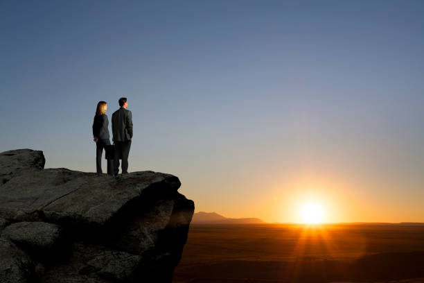 Business People Standing On Cliff Looking Into Sunset