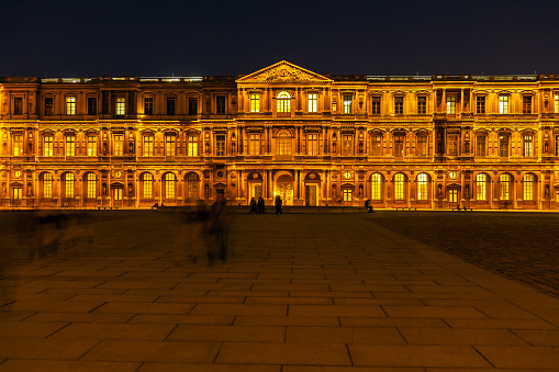 People have a rest in front of the Louvre Palace and Pyramid at night