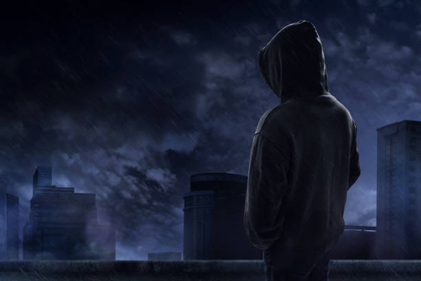uomo in piedi sul tetto in una notte piovosa - uomo incappucciato foto e immagini stock