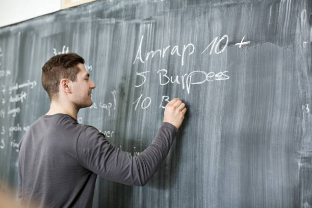 Professional fitness coach writing instructions on blackboard Professional fitness coach writing the cross training workout instructions on blackboard at gym gym chalkboard stock pictures, royalty-free photos & images