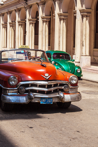 HAVANA, CUBA - APRIL 1, 2012: Taxi driver greets tourists on Orange Cadillac Series 62 cabriolet