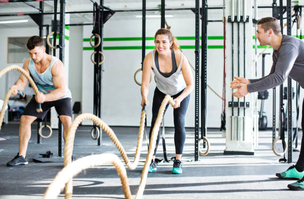 Fitness people working out with battle ropes Fitness gym with man and woman working out with battle ropes at the gym with trainer battle stock pictures, royalty-free photos & images