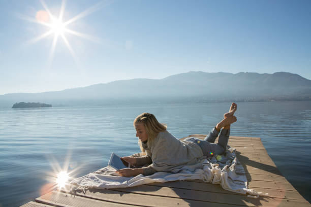 istock Young woman relaxing on lake pier with digital tablet 641795054