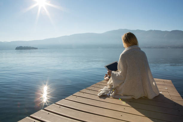 istock Young woman relaxing on lake pier with digital tablet 641795168